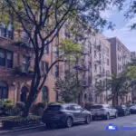 Dream Moving image of older apartment buildings in Queens on a tree-lined residential street with brick facades, fire escapes, and parked cars.